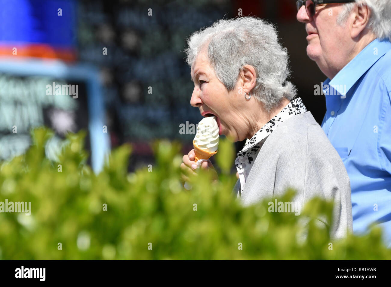 Coppia senior a camminare su una passeggiata in una calda giornata di primavera nel Regno Unito, mangiare gelati. Foto Stock