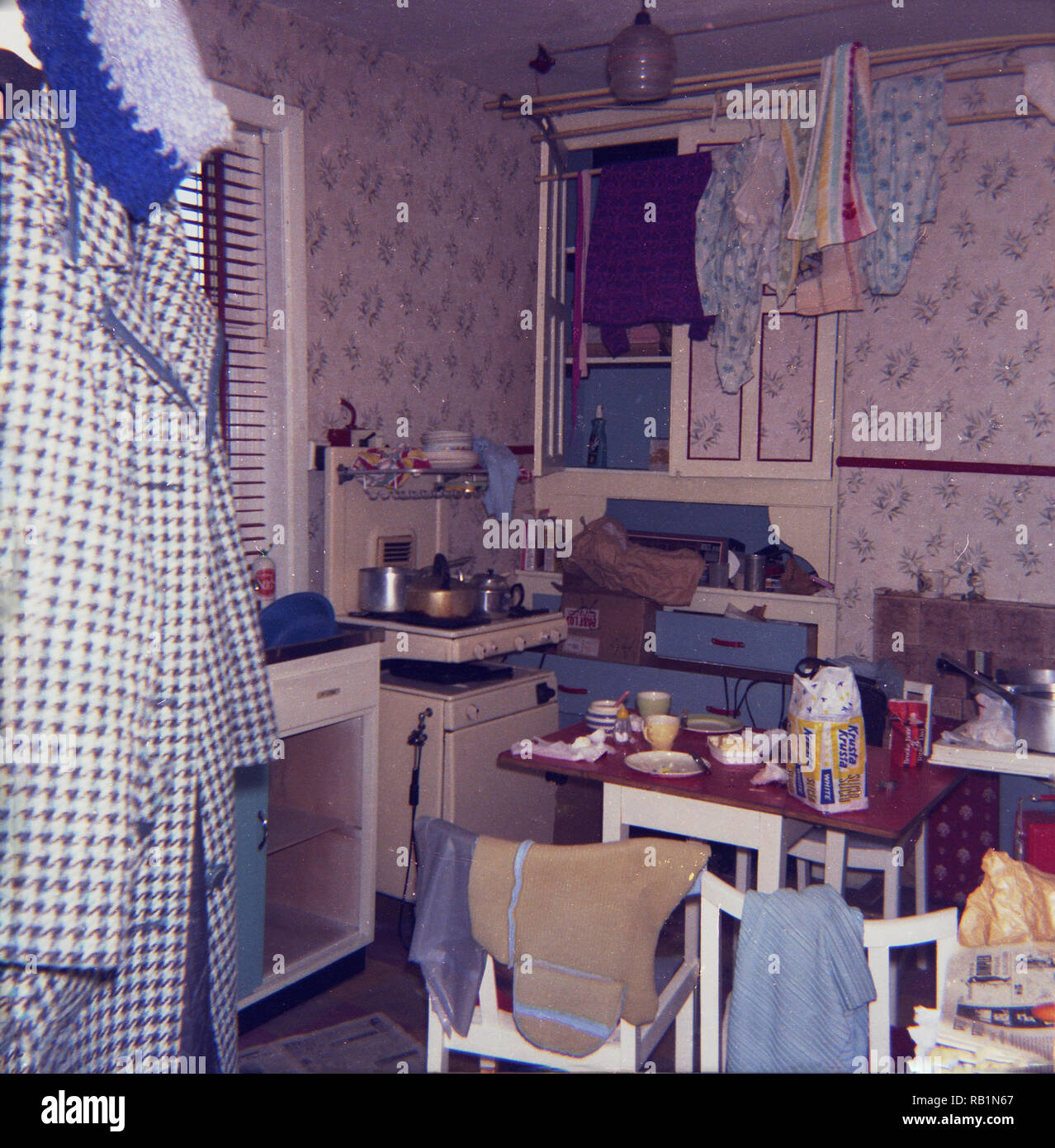 Anni Settanta, storico, una piccola cucina ingombra, che presentano i prodotti sparsi intorno e un capi appesi o linea di lavaggio. Foto Stock