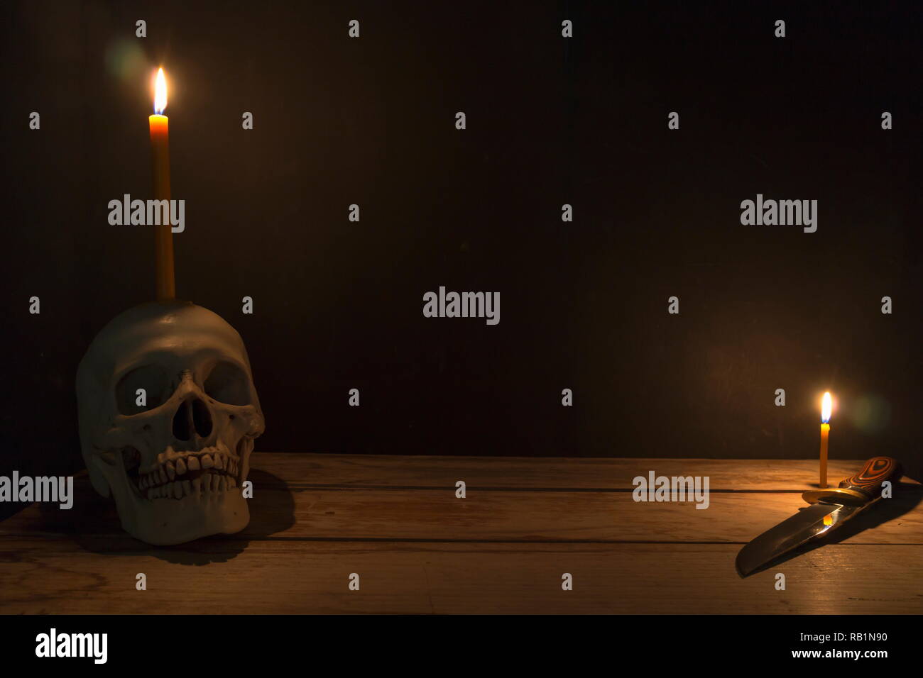 Cranio umano con la luce di una candela e il coltello sul tavolo di legno in uno sfondo scuro, decorare per tema Halloween con copia spazio. Foto Stock