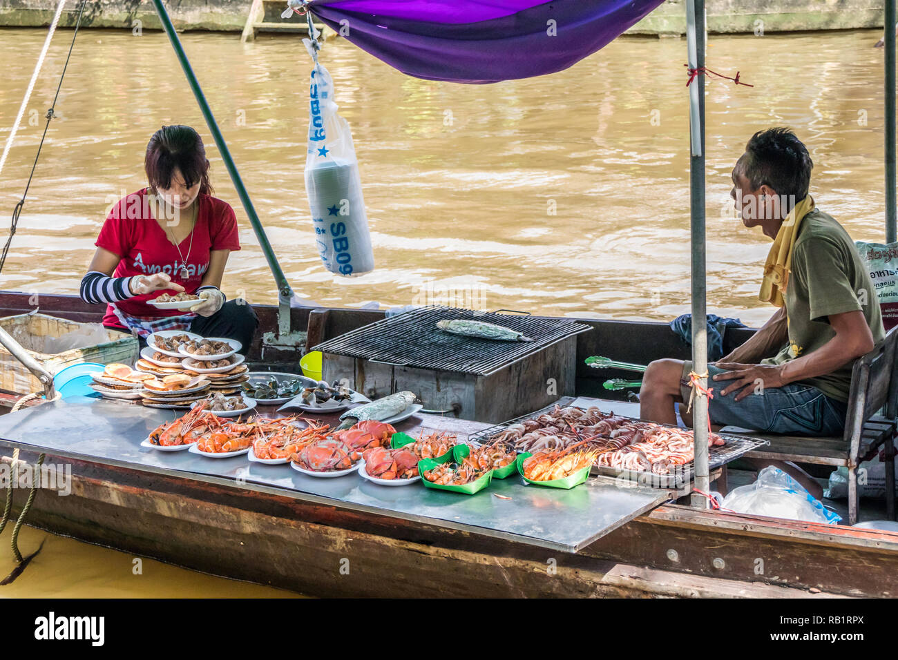 Amphawa, Tailandia - 7 Ottobre 2018: la cottura alla griglia e la vendita di frutti di mare da una barca, un mercato galleggiante si svolge ogni fine settimana. Foto Stock