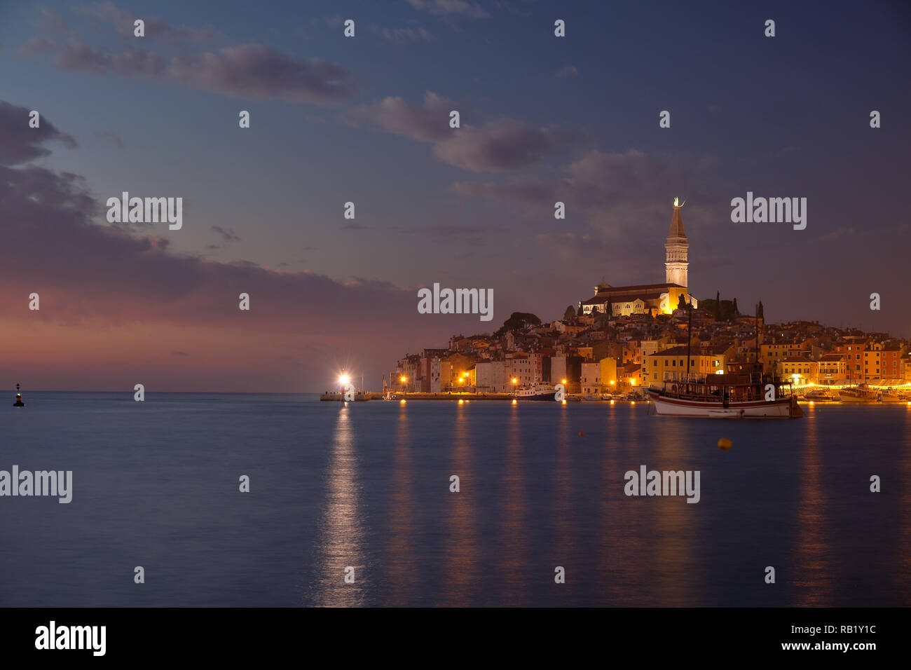 Vista della città di Rovigno in Croazia. La luce blu al tramonto con le luci della città in fase di accensione. Sfocata barche di movimento dalla lunga esposizione Foto Stock