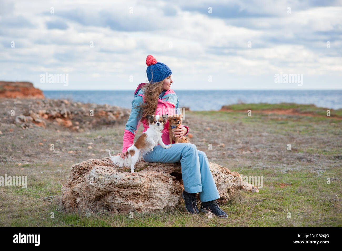 Bella giovane donna in hat e tuta insieme con due cani sulla riva del mare Foto Stock