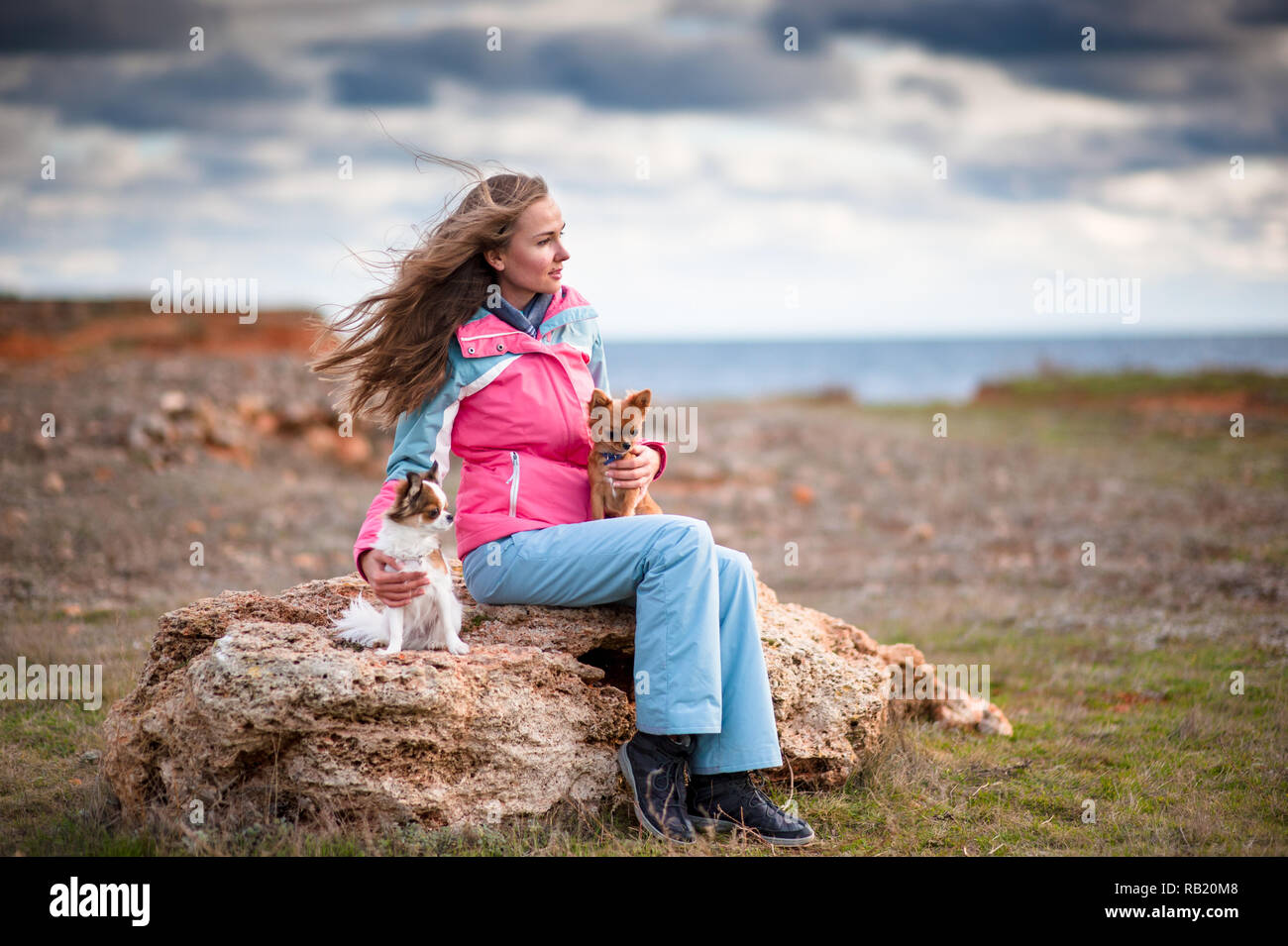Piuttosto giovane donna in tuta seduto con due cani riva del mare in condizioni di clima freddo Foto Stock
