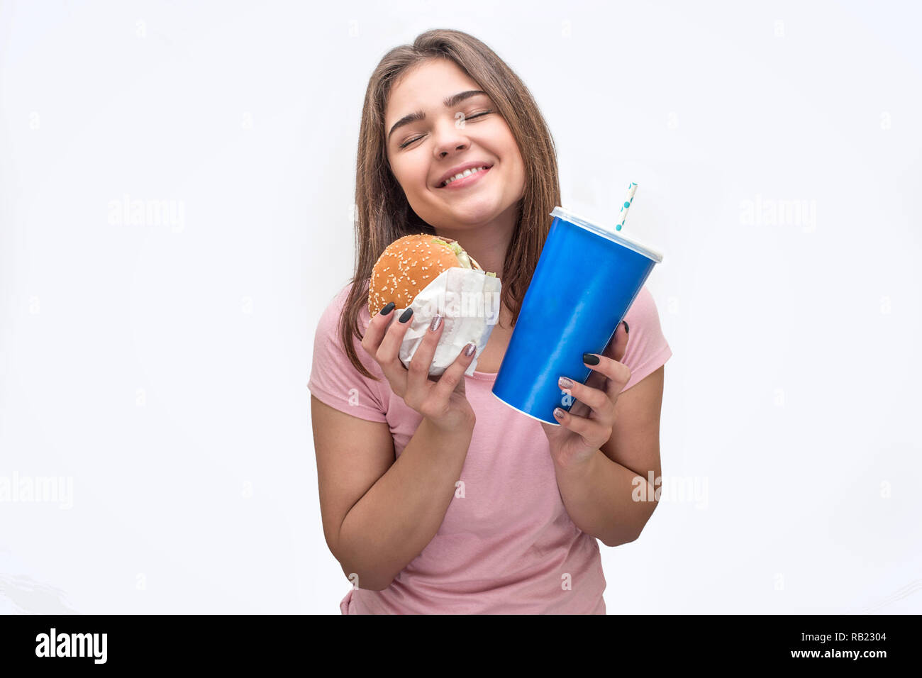 Allegra e felice giovane donna attesa burger e bicchiere di coca-cola in mani. Ella ha un aspetto straordinario. Isolato su sfondo bianco. Foto Stock