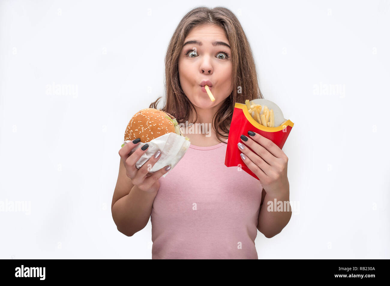Stupito i giovani guardano sulla fotocamera e mangiare patatine fritte. Ella tenere burger in mani come bene. Isolato su sfondo grigio. Foto Stock