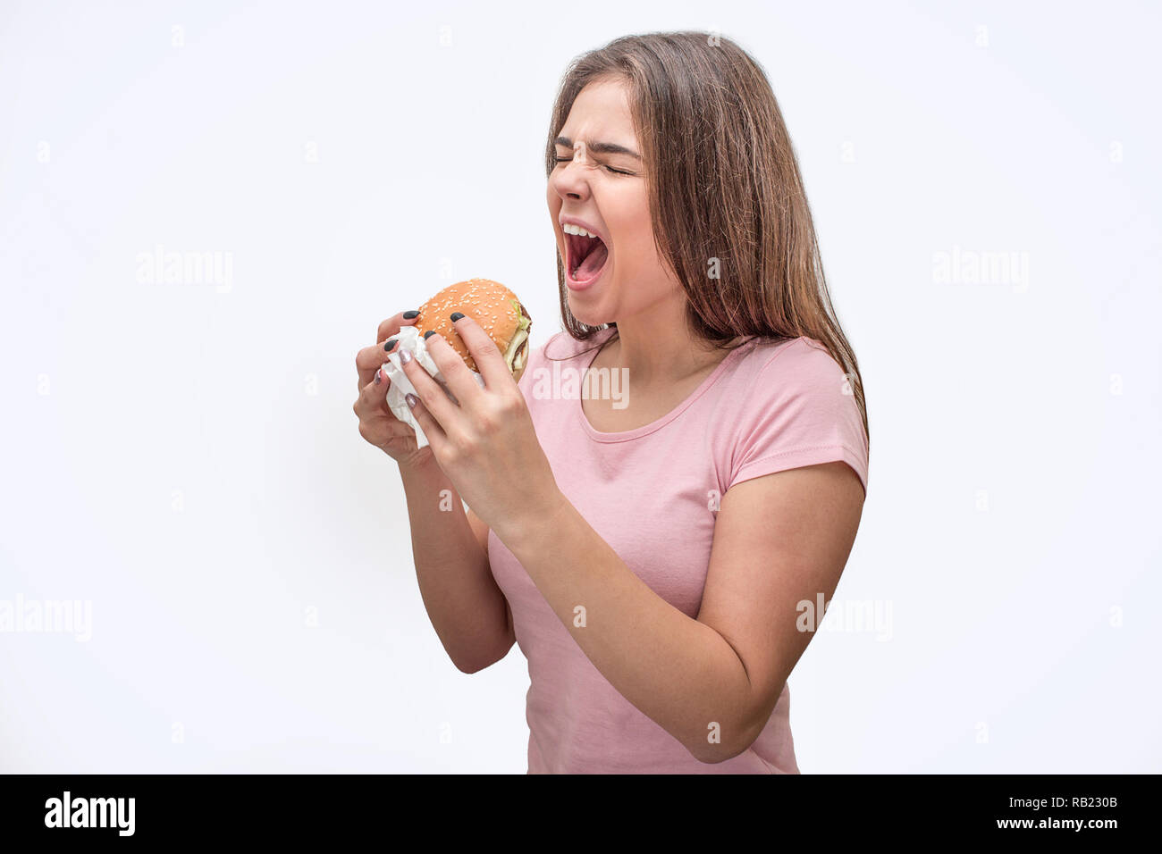 Giovani donne Tieni la bocca aperta. Ella tenere burger in mani. Modello è di andare a mangiare. Isolato su sfondo grigio. Foto Stock