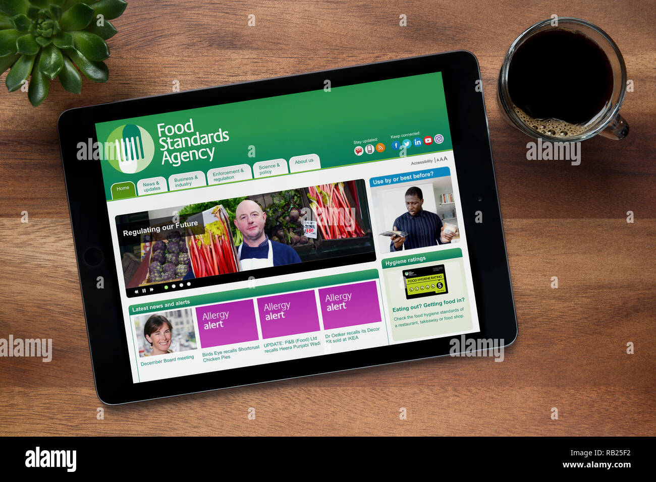 Il sito web della Food Standards Agency è visto su un tablet iPad, su di un tavolo di legno lungo con un caffè espresso e una pianta di casa (solo uso editoriale) Foto Stock