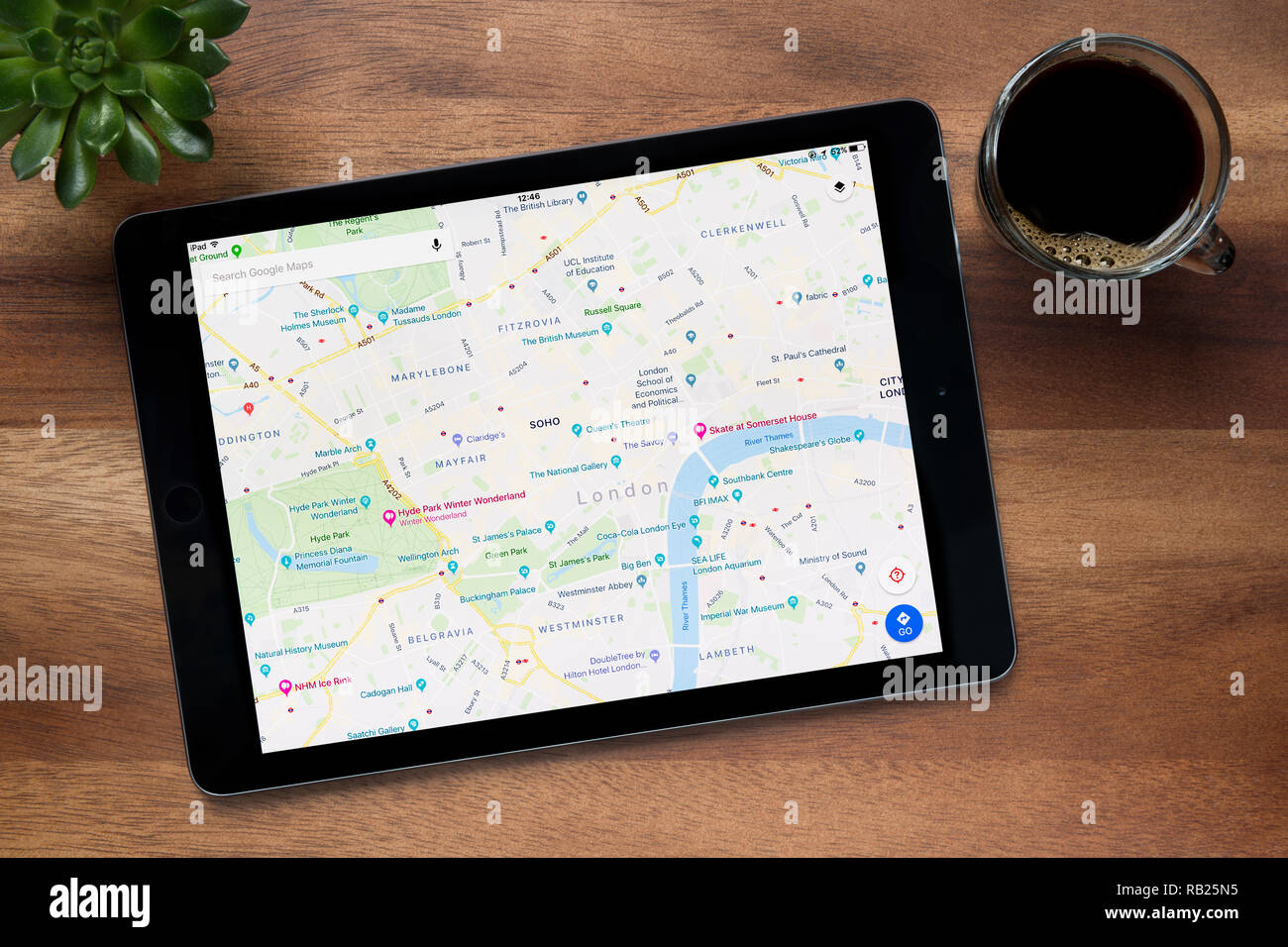 Il sito web di Google Maps è visto su un tablet iPad, su di un tavolo di legno lungo con un caffè espresso e una pianta di casa (solo uso editoriale). Foto Stock