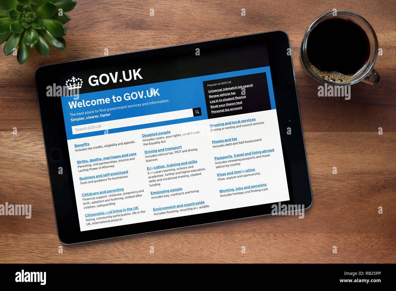 Il sito web del governo del Regno Unito è visto su un tablet iPad, su di un tavolo di legno lungo con un caffè espresso e una pianta di casa (solo uso editoriale). Foto Stock
