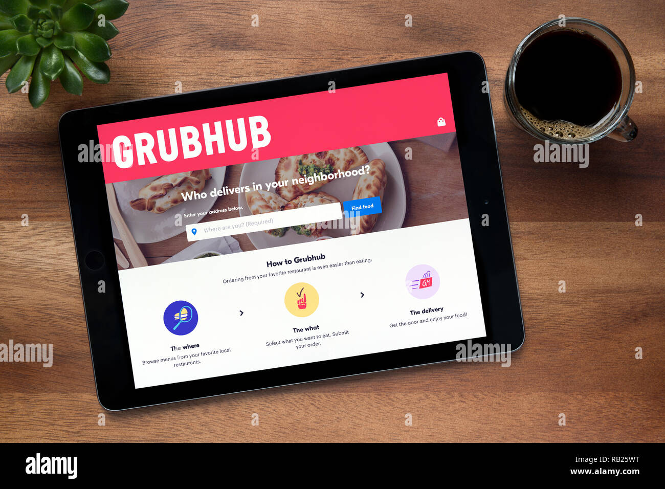 Il sito web di GrubHub è visto su un tablet iPad, su di un tavolo di legno lungo con un caffè espresso e una pianta di casa (solo uso editoriale). Foto Stock