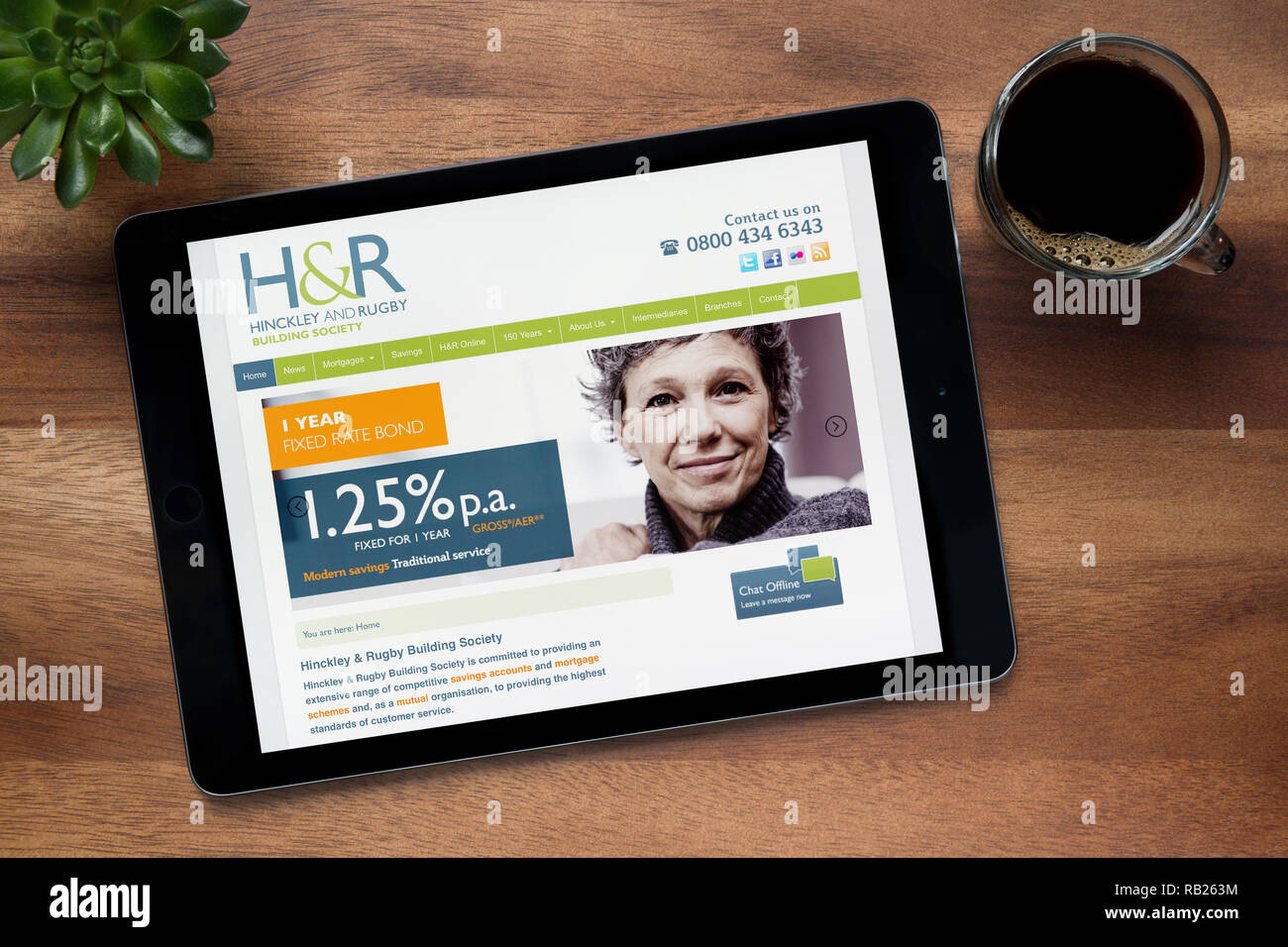 Il sito web di Hinckley & Rugby è visto su un tablet iPad, su di un tavolo di legno lungo con un caffè espresso e una pianta di casa (solo uso editoriale). Foto Stock
