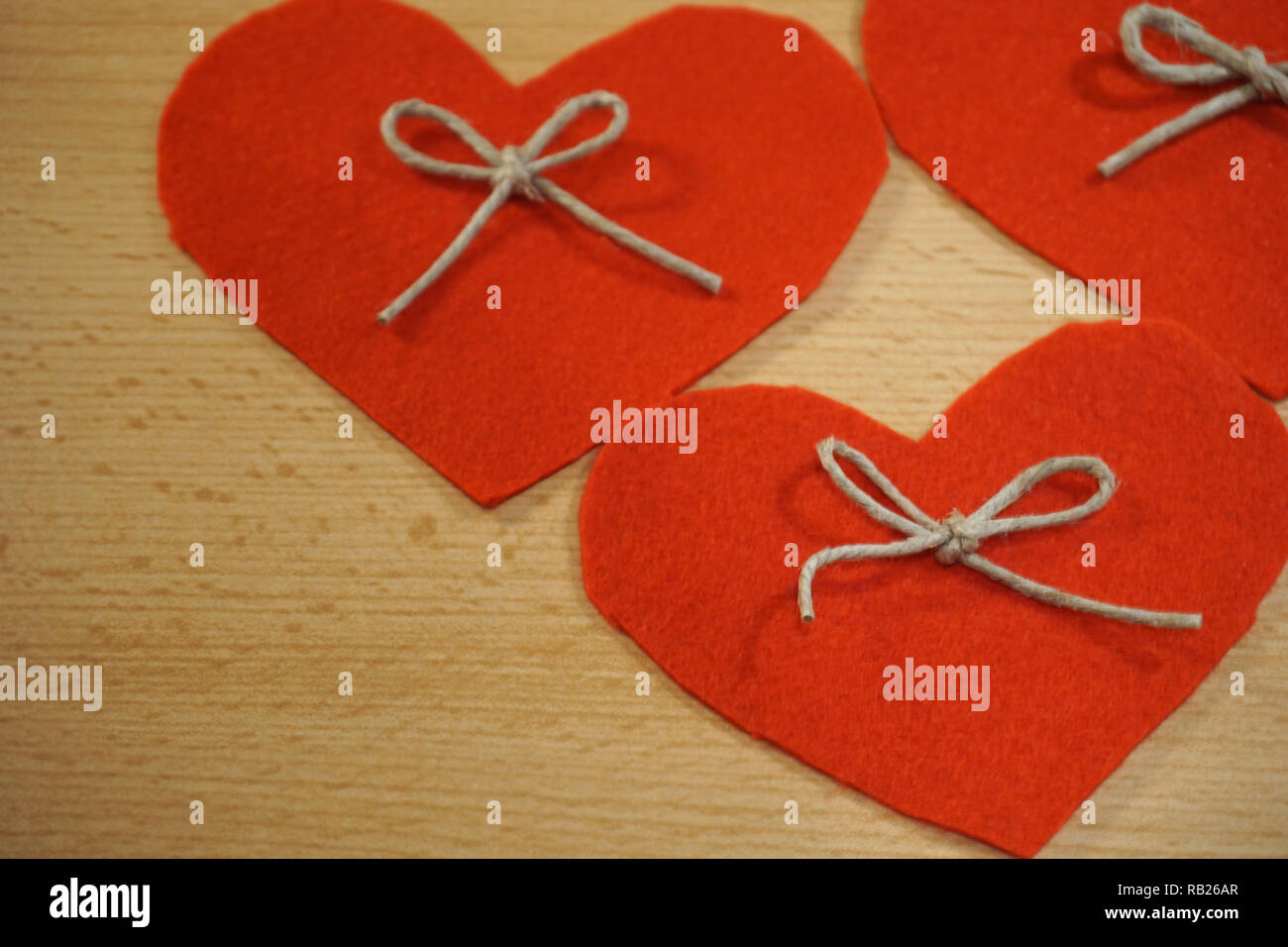 Tre cuori rossi realizzata in tessuto decorato con corda di lino bow su sfondo di legno Foto Stock