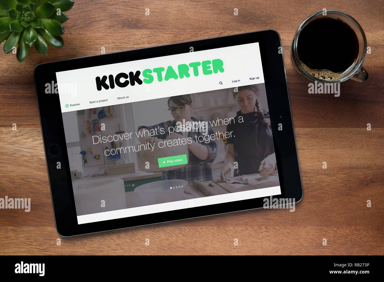 Il sito web di Kickstarter è visto su un tablet iPad, su di un tavolo di legno lungo con un caffè espresso e una pianta di casa (solo uso editoriale). Foto Stock