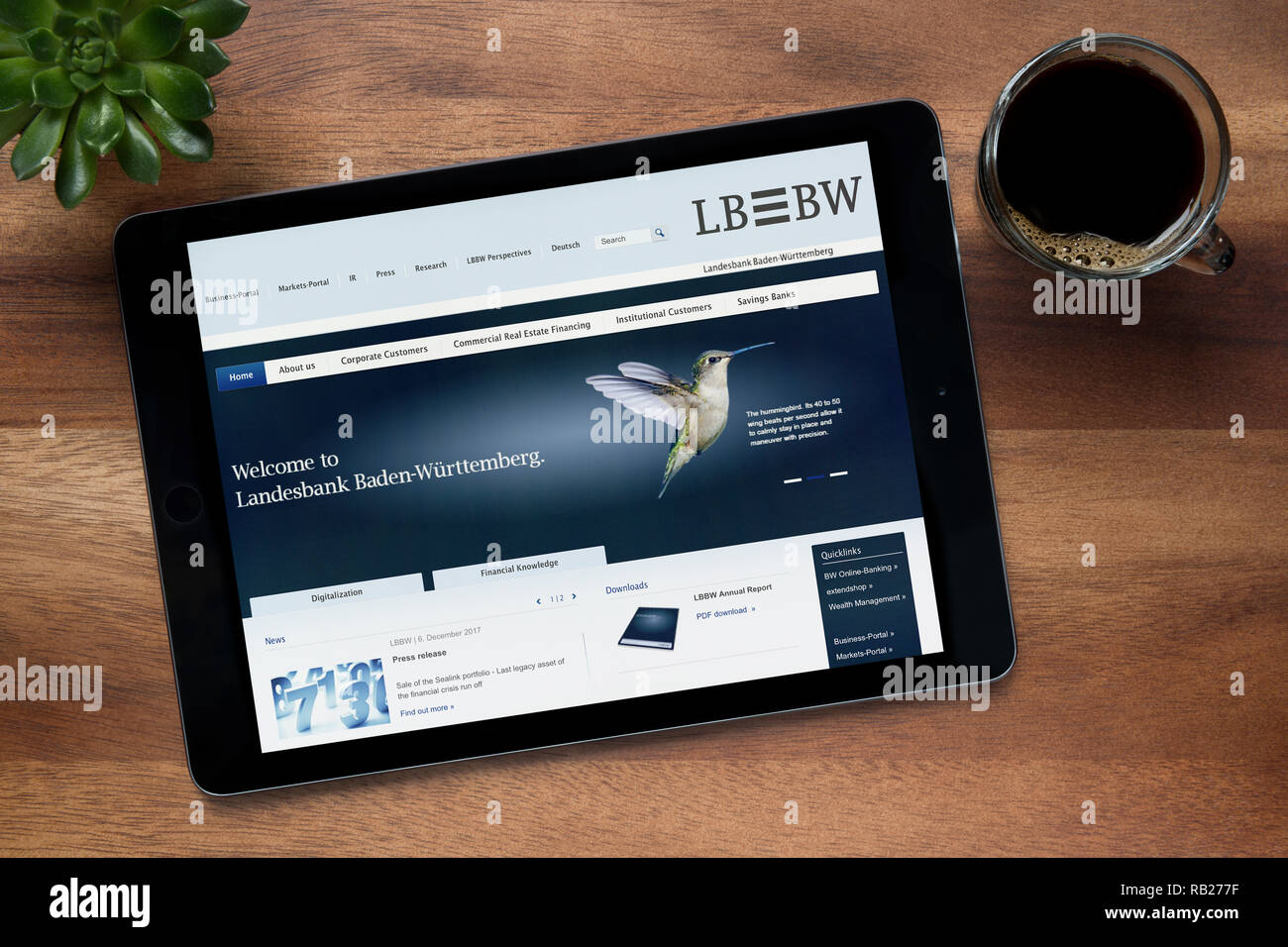 Il sito web di LB BW è visto su un tablet iPad, su di un tavolo di legno lungo con un caffè espresso e una pianta di casa (solo uso editoriale). Foto Stock