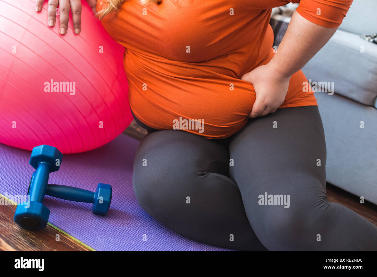 Chubby donna lo sport a casa seduto appoggiato sulla sfera holding fat piegare close-up Foto Stock