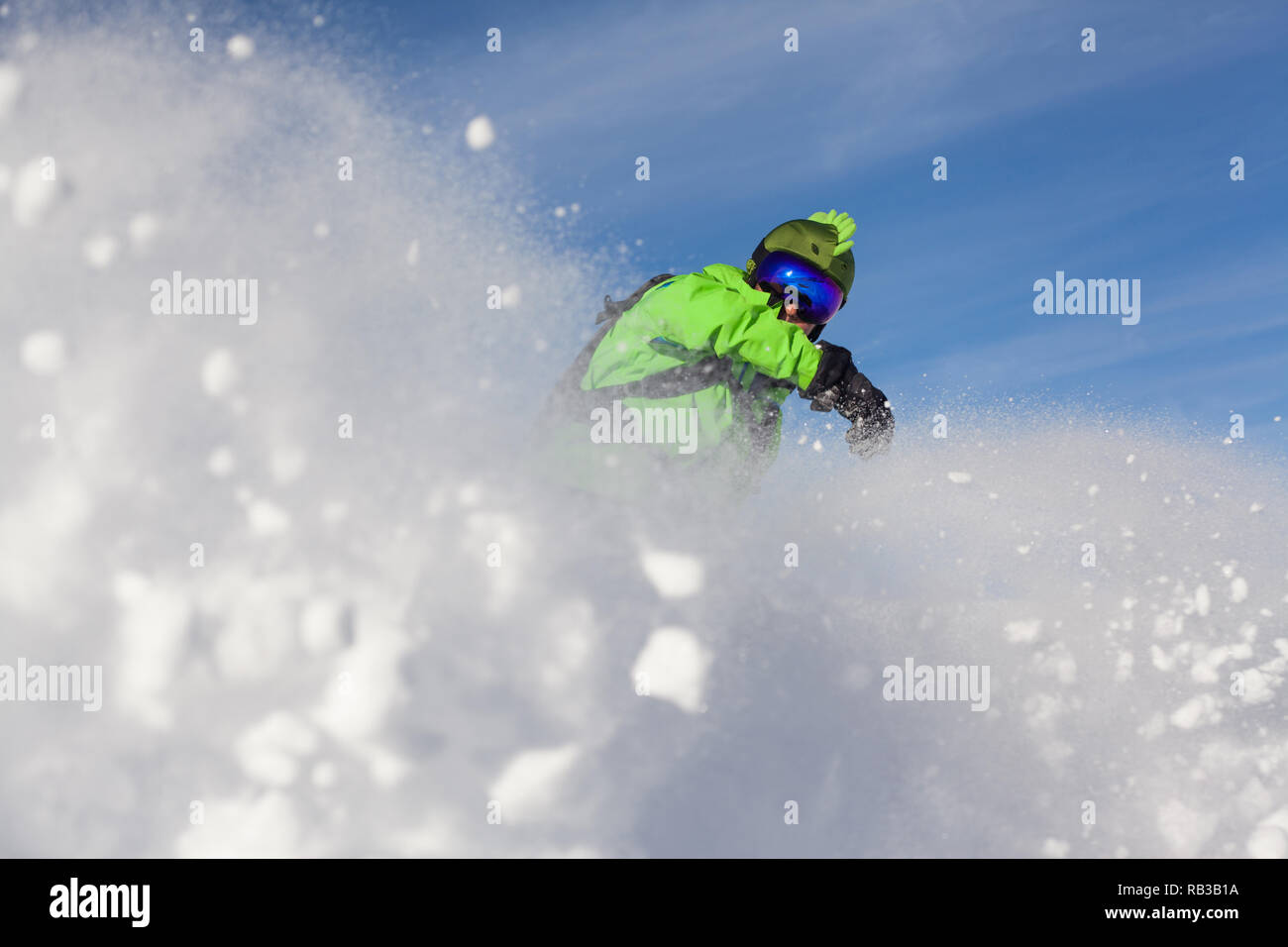 Snowboarder vestito in verde sollevando la neve mentre cancellando contro blu cielo sereno sulle pendici delle Alpi in Francia. Foto Stock