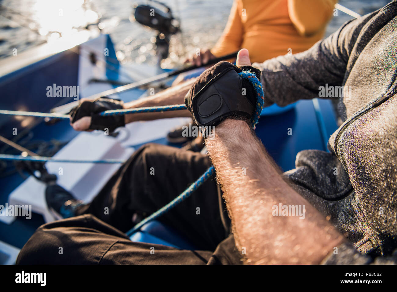 Close-up del maschio in mani guanti tirando la corda della barca a vela  mentre yacht di ormeggio e di seduta con gli amici sul ponte Foto stock -  Alamy