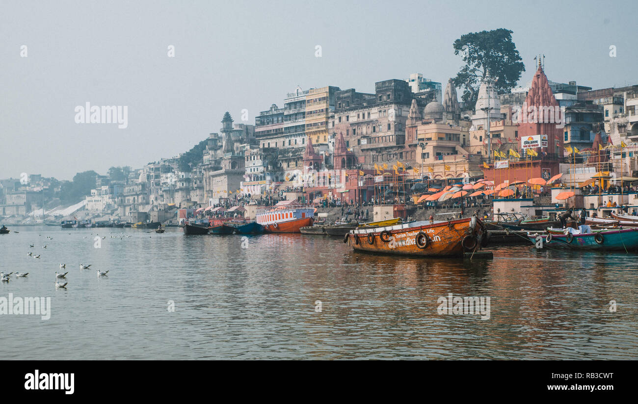 Il paesaggio della città vecchia Varanasi in India del nord. Facendo una gita in barca sul fiume santo Ganges chiamato ganga. Edifici di colore arancione e barche Foto Stock