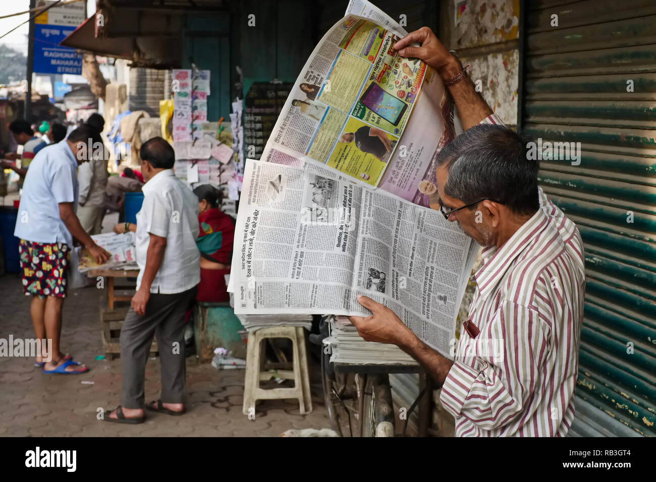 Un appassionato lettore di giornali in Mumbai, India, la lettura di una lingua locale carta; edizioni a stampa di quotidiani sono ancora molto popolari in India Foto Stock