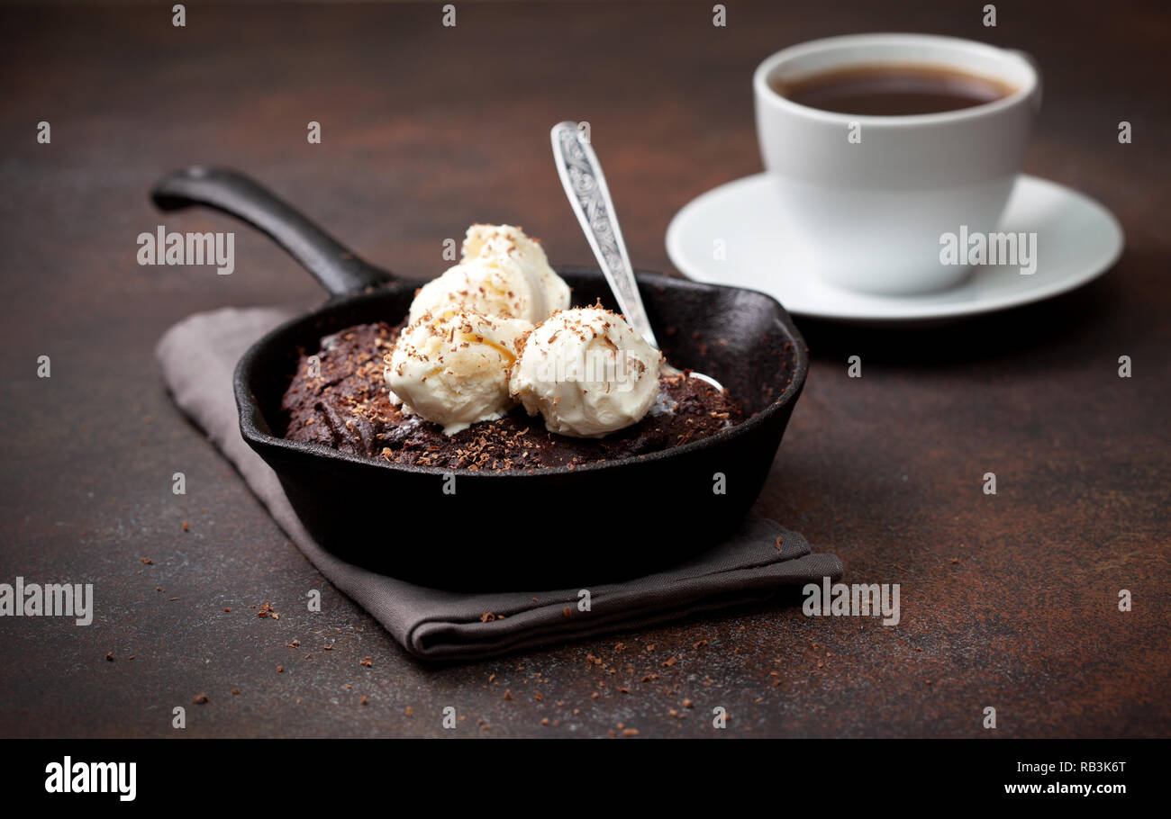 Brownie con gelato alla vaniglia in una padella, una tazza di caffè su uno sfondo marrone Foto Stock