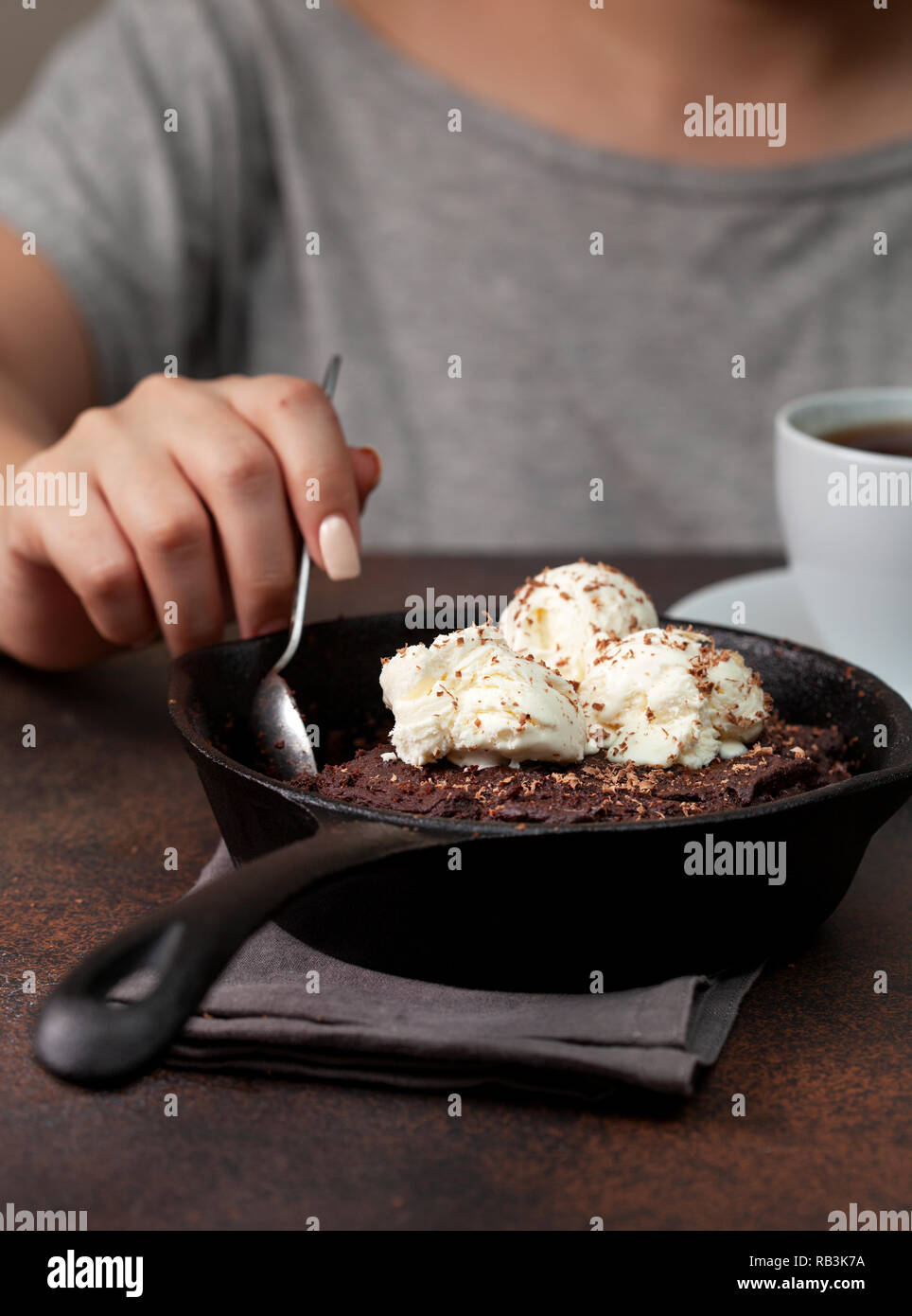 Brownie con gelato alla vaniglia in una padella, una tazza di caffè su uno sfondo marrone Foto Stock
