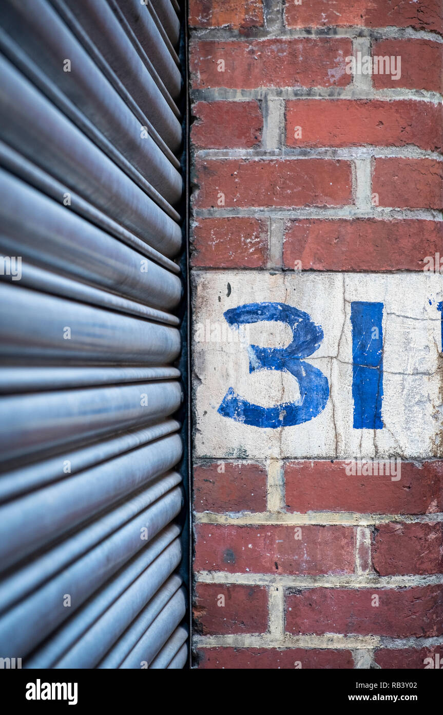 Il numero 31 dipinta a mano su un muro di mattoni con un rullo porta in primo piano Foto Stock
