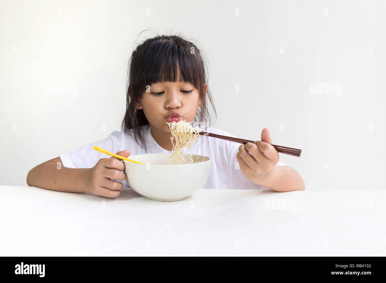 Ritratto di ragazzo asiatico ragazza mangiare spaghetti istantanei con il bianco tavolo in legno e sfondo bianco. Foto Stock