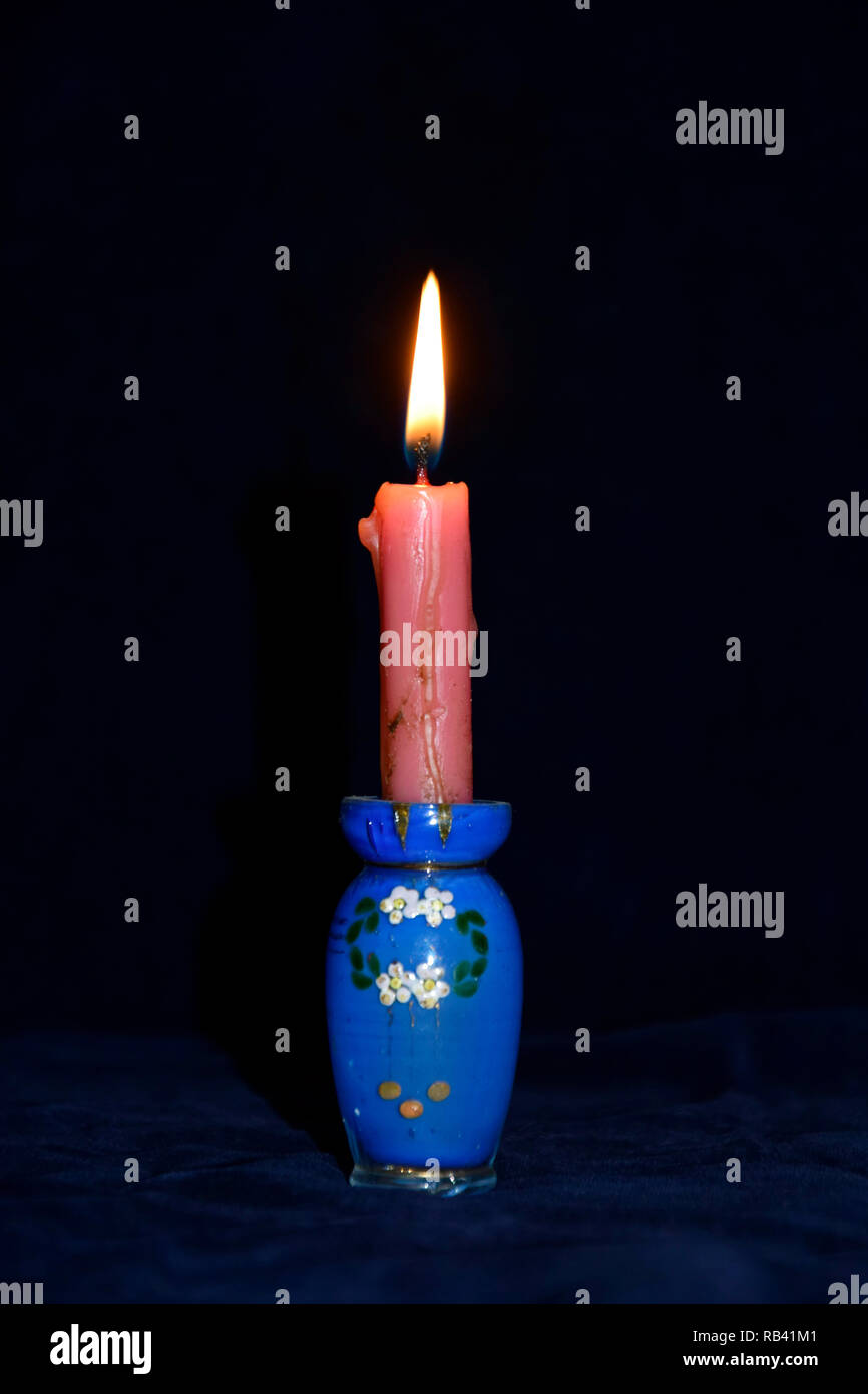 Illuminato di candela rossa in vetro blu portacandele, con blu scuro che circonda Foto Stock