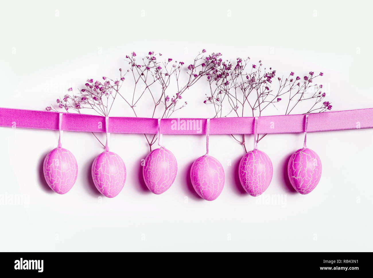 Neon Pink uova di Pasqua appeso al nastro a muro bianco sullo sfondo Foto Stock