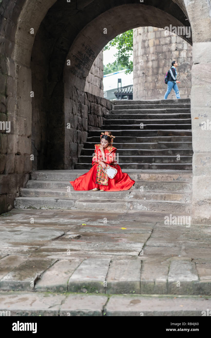 Donna in rosso vestito tradizionale seduta sul passo del molo, Chongqing , Cina Foto Stock