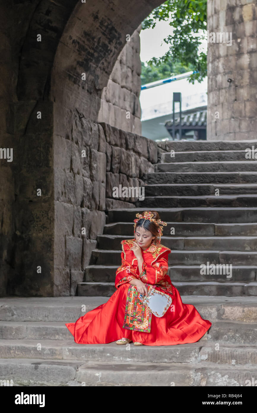 Donna in rosso vestito tradizionale seduta sul passo del molo, Chongqing , Cina Foto Stock