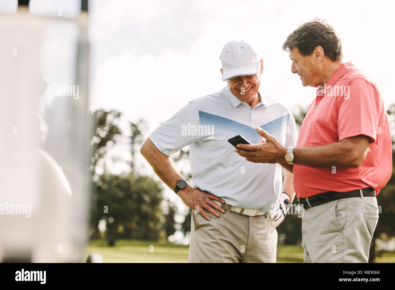 Due giocatori di golf in piedi insieme utilizzando il telefono cellulare. Senior golfisti guardando i punteggi sul telefono dopo il gioco sul campo da golf. Foto Stock