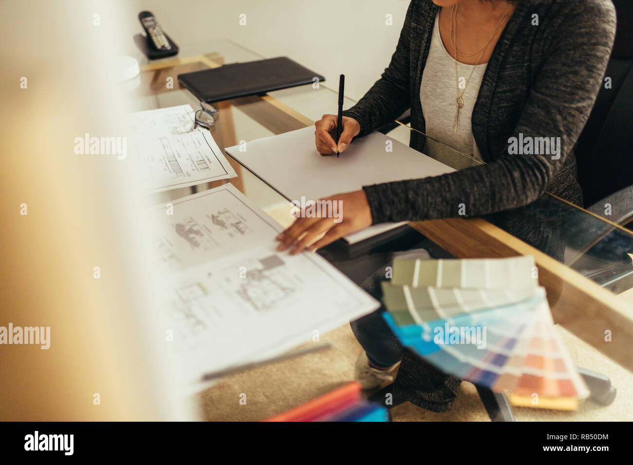 Architetto femmina la preparazione di un nuovo piano di pavimento con riferimento di una bozza di progetto di alloggiamento. Donna designer che lavorano su progetti di nuovo alla sua scrivania. Foto Stock