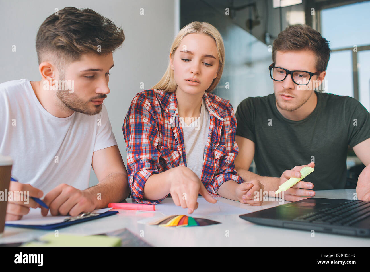 Grave giovane donna punto sul colore pallete. Due ragazzi guardare. I colleghi seduti a tavola insieme in una stanza. Essi lavorano. Foto Stock