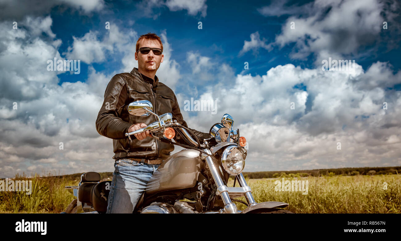 Biker uomo che indossa una giacca di pelle e occhiali da sole seduto su una motocicletta Foto Stock