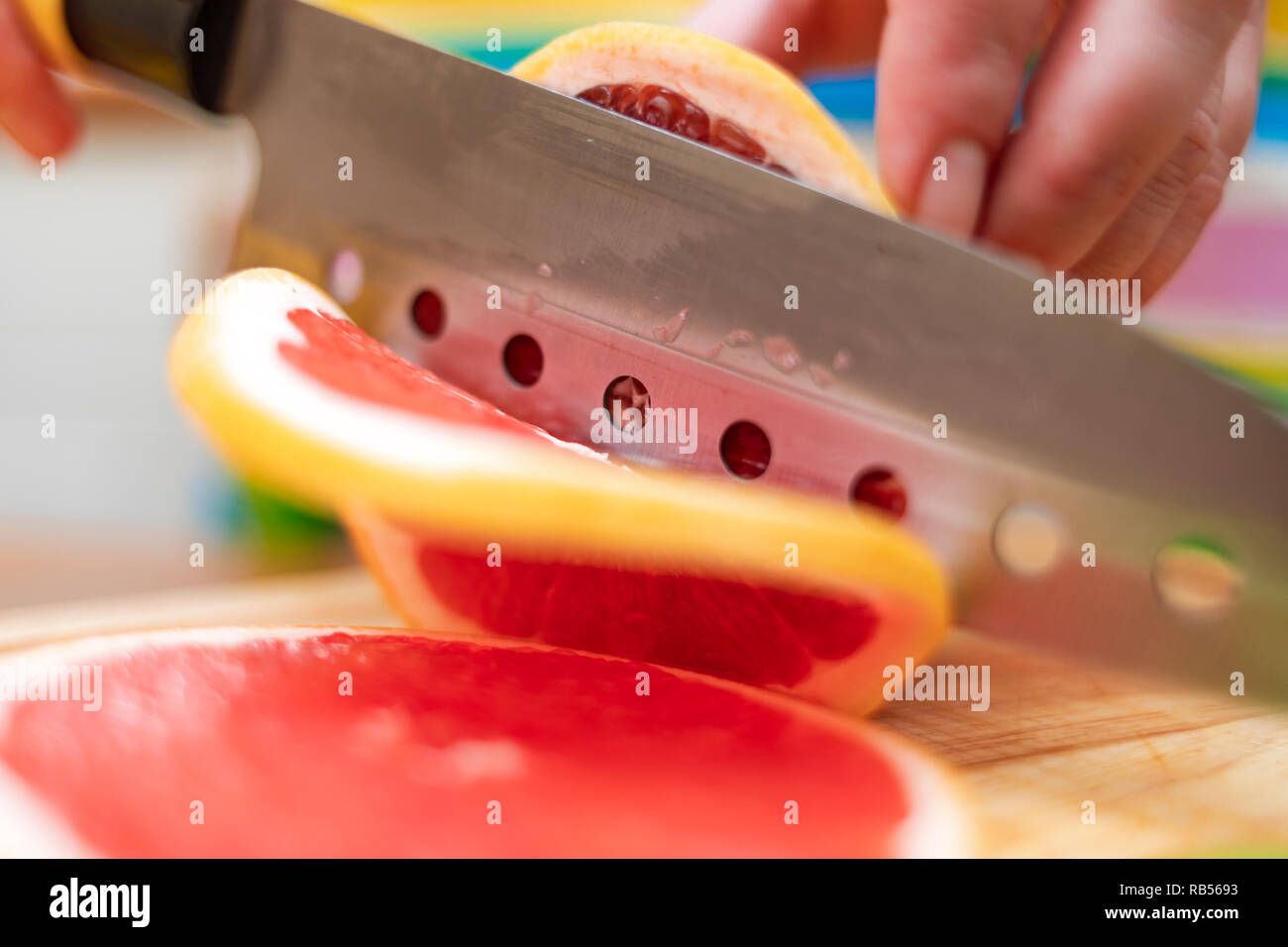 Le mani delle donne casalinghe tagliate con un coltello succo di pompelmo fresco sul bordo di taglio della tabella di cucina Foto Stock