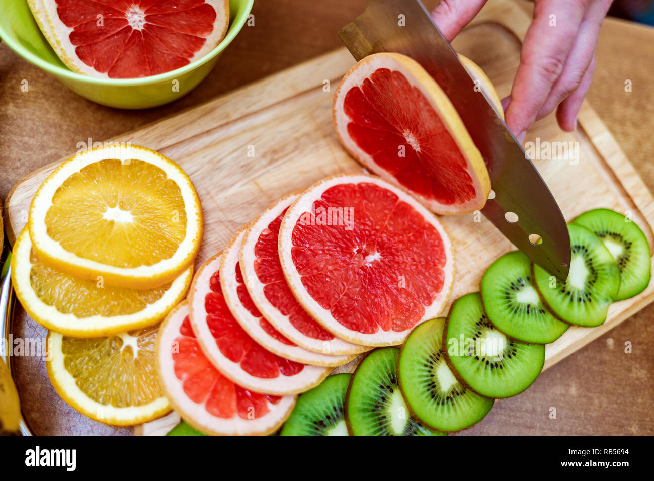 Le mani delle donne casalinghe tagliate con un coltello succo di pompelmo fresco sul bordo di taglio della tabella di cucina Foto Stock