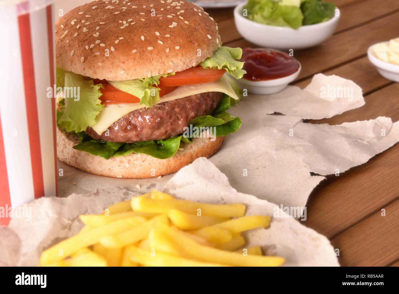 Hamburger di manzo con formaggio e pomodori su carta con chip su un tavolo di legno. Vista in elevazione. Composizione orizzontale. Foto Stock
