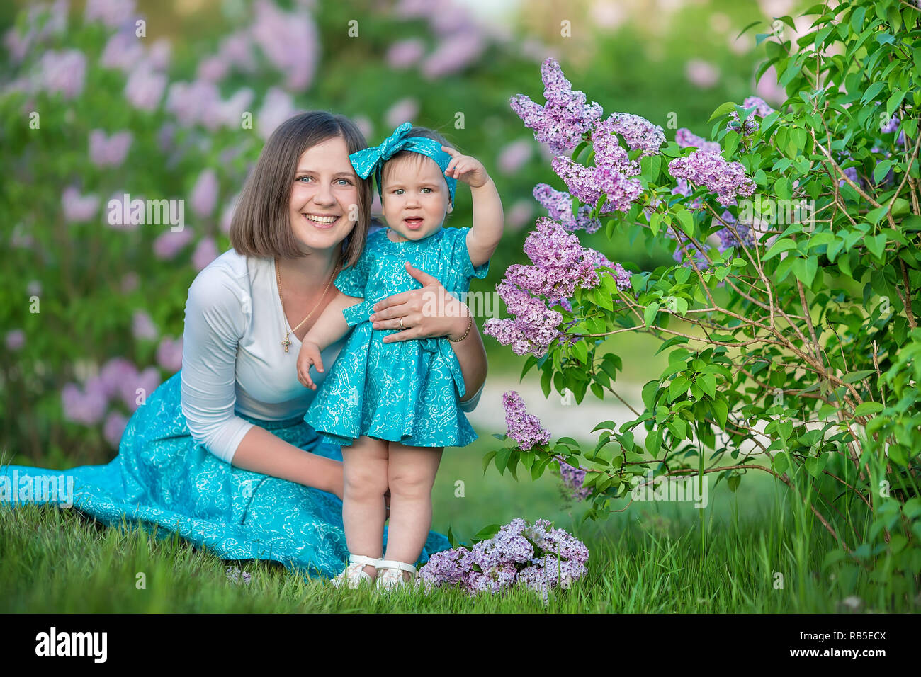 Felice madre mom con la figlia godendo di tempo su un posto eccezionale tra la siringa lilla bush.Giovane Donna con cesto pieno di fiori vestito in jeans un Foto Stock