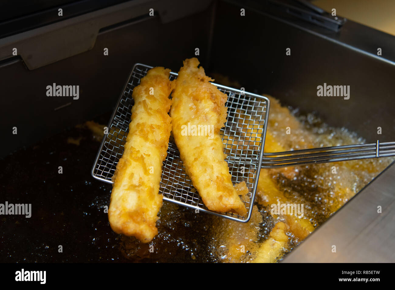 Due pezzi di merluzzo bianco sollevato fuori di una friggitrice in un chip shop nel Regno Unito. Foto Stock