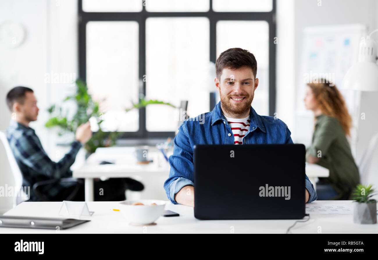 Sorridente uomo creativo con il computer portatile lavorando in ufficio Foto Stock