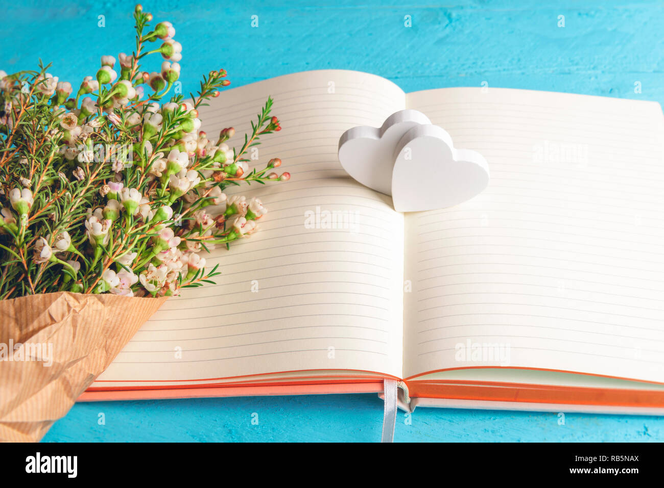 Piccoli fiori bianchi bouquet su un notebook vuota e due cuori di legno, su sfondo blu. Il giorno di San Valentino regali aziendali. Momenti felici contesto. Anniversario. Foto Stock