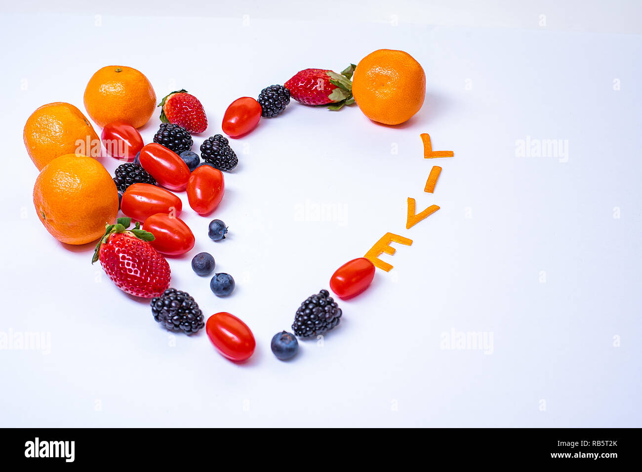 A forma di cuore la disposizione dei frutti con la parola vivere fatta di bucce di mandarino in un pulito lo sfondo bianco con copia spazio. Foto Stock