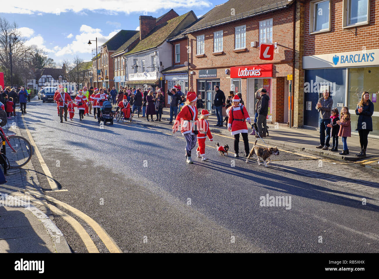 La gente vestita come Santa Claus e i loro cani prendendo parte alla grande Thatcham Santa Fun Run in Thatcham high street mentre la gente guarda su Foto Stock