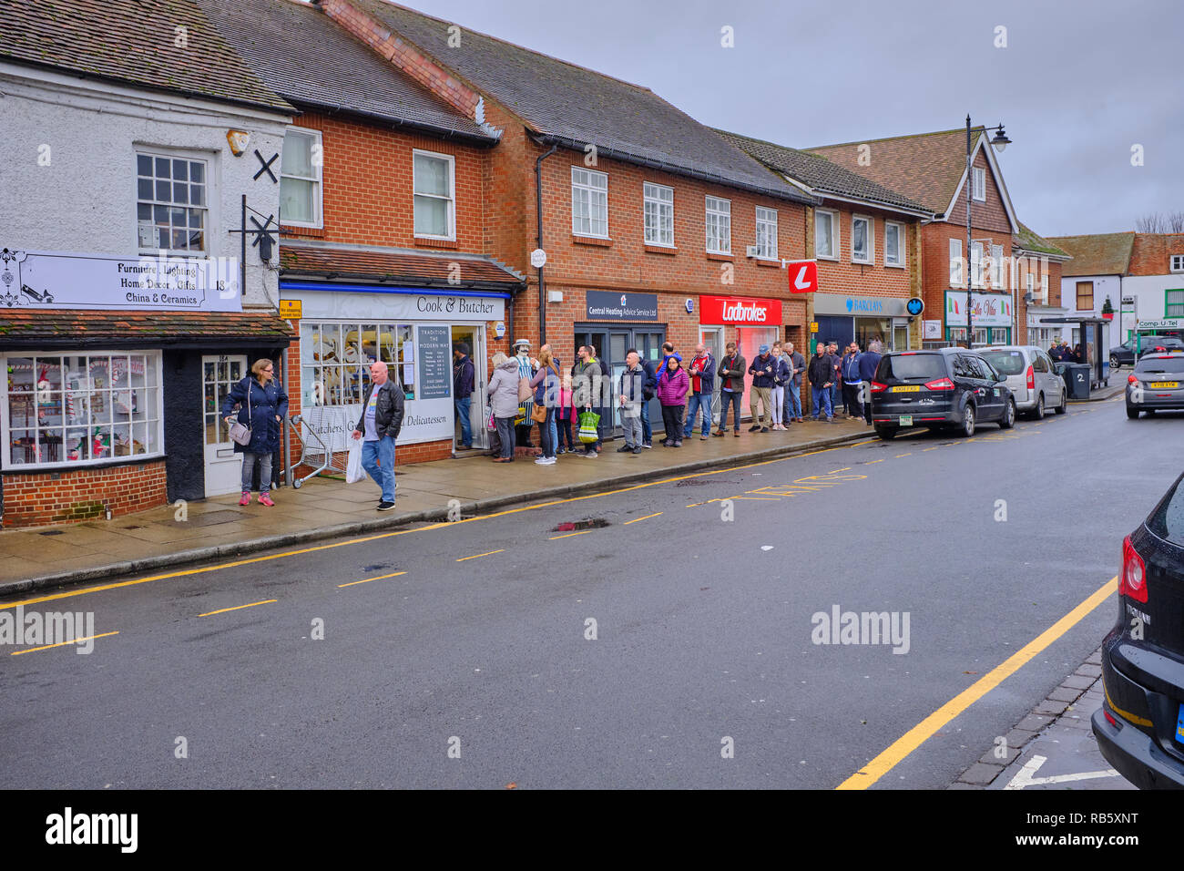 Una lunga fila di persone sul marciapiede in attesa di entrare il macellaio locale negozio vicino a Natale a Thatcham high street, Berkshire, Regno Unito Foto Stock
