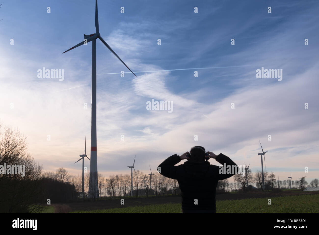 Uomo di fronte una fattoria eolica utilizza la protezione del rumore per ridurre il rumore della turbina eolica Foto Stock