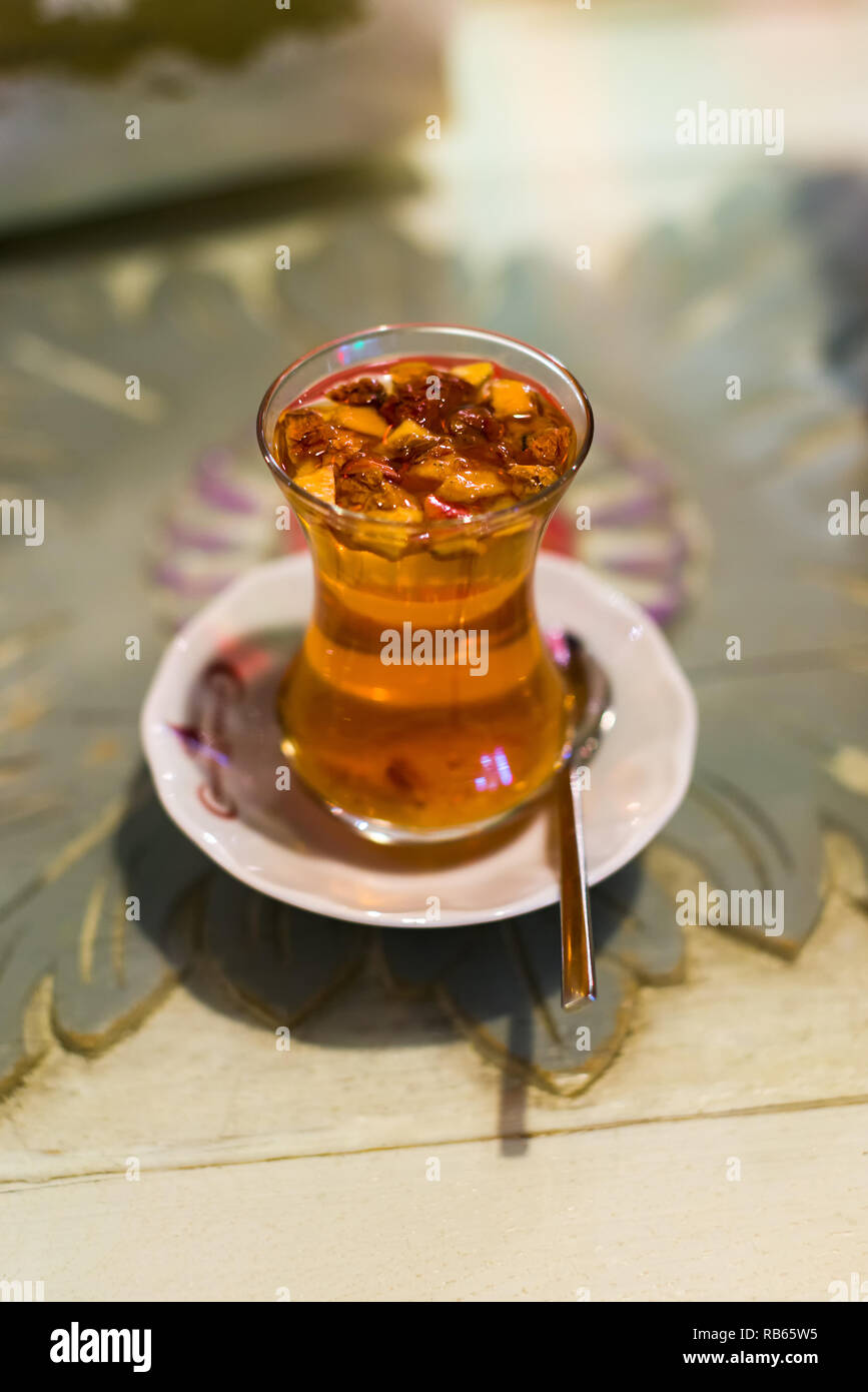 Un vetro trasparente tazza di turco tradizionale tè apple con i bit di apple floating nella bevanda su un piattino bianco con cucchiaino, Istanbul, Turchia Foto Stock