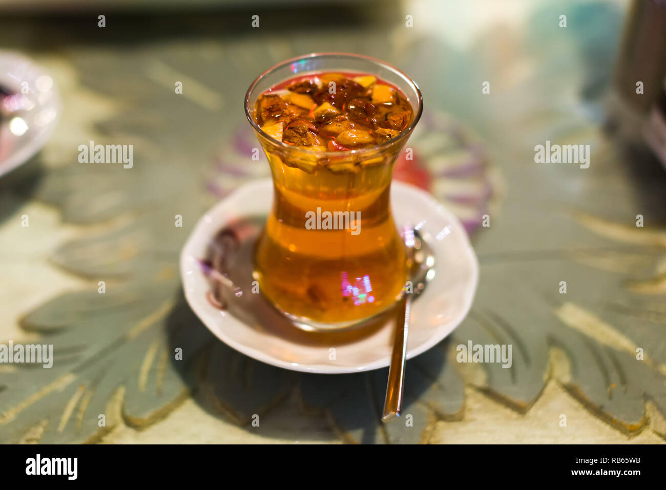 Un vetro trasparente tazza di turco tradizionale tè apple con i bit di apple floating nella bevanda su un piattino bianco con cucchiaino, Istanbul, Turchia Foto Stock
