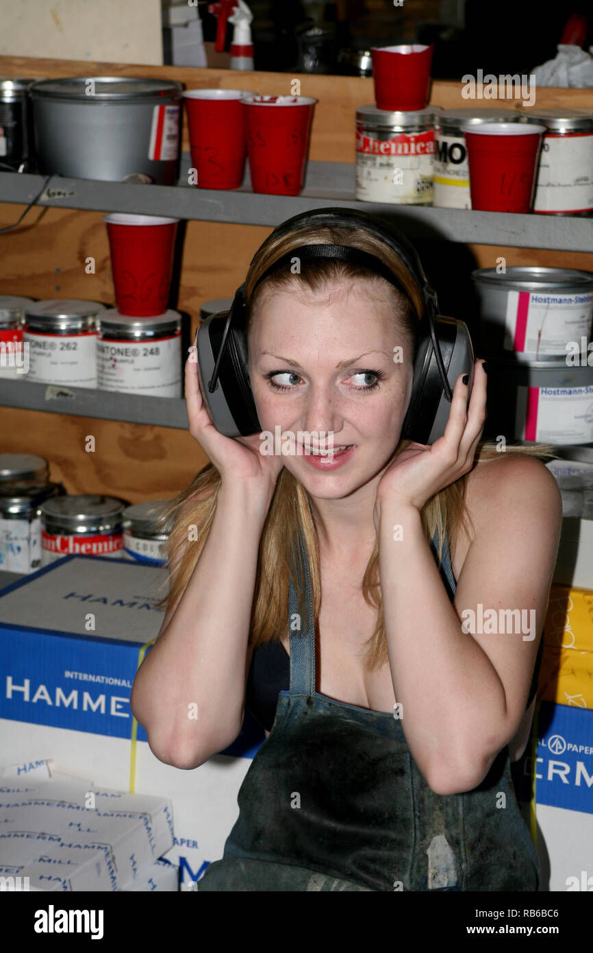 Donna bionda che indossa un grembiule protettivo durante il lavoro nel negozio di stampa e ascolto di musica con cuffie di lei Foto Stock