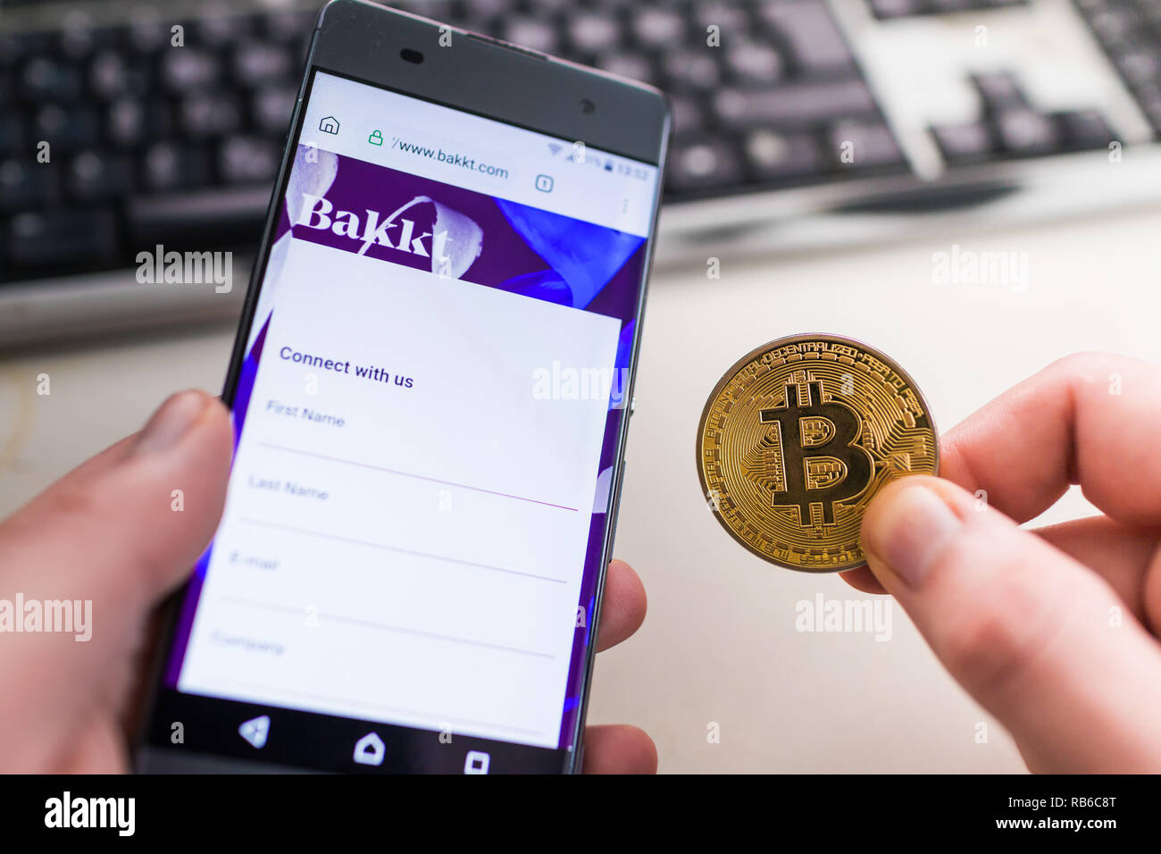 SLOVENIA - Gennaio 8, 2019: uomo azienda Bitcoin monete e in altra parte smartphone con aperto Bakkt sito web. Foto Stock